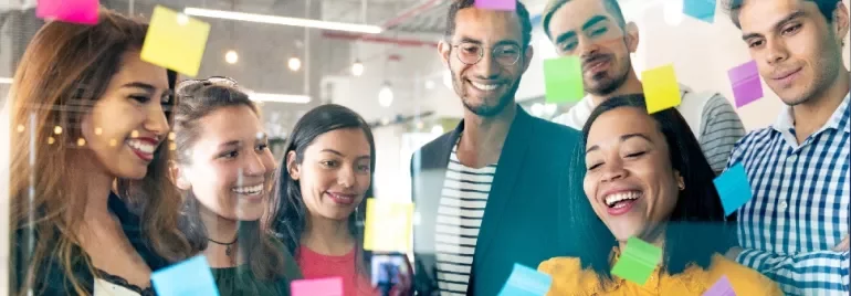 A group of diverse colleagues brainstorming with colorful sticky notes on a glass wall.