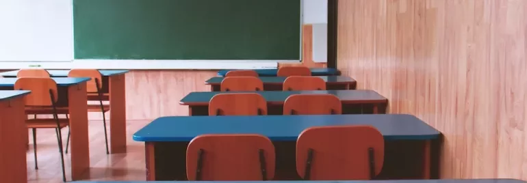 Empty classroom with wooden desks and a green chalkboard.