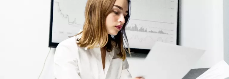 Woman in white shirt reviewing documents in front of graph.