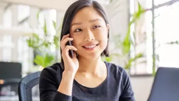 Woman smiling while on a phone call in a modern office.