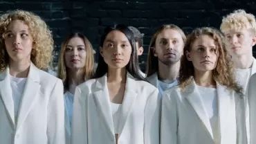 A group of people in white suits standing against a dark background.