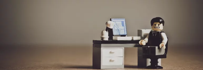 Lego figure at a desk with a computer, looking distressed.