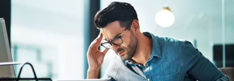 Man in glasses working on a laptop, looking focused in casual office setting.
