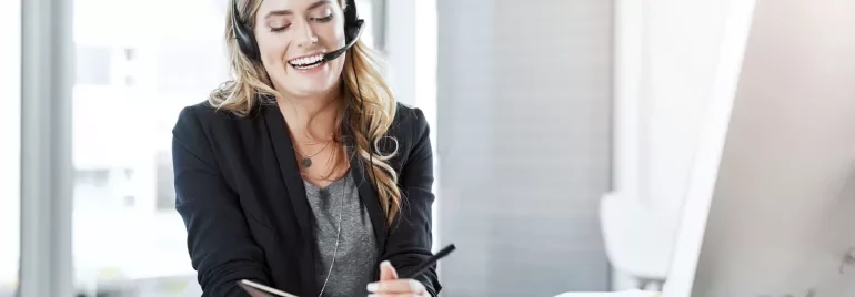 A woman wearing a headset holds a notepad, engaged in a discussion or taking notes.
