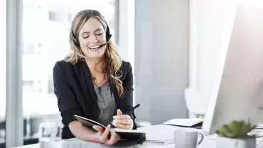 A woman wearing a headset holds a notepad, engaged in a discussion or taking notes.