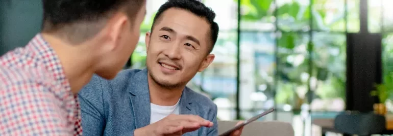 A male professional holding a tabelt and in discussion with another male professional