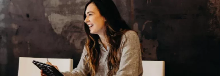 Woman smiling while holding a tablet at a wooden table