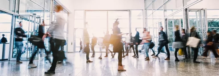 Blurry crowd of people walking through a modern office building entrance.