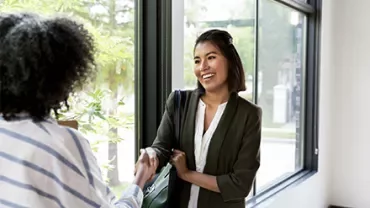 Two women shaking hands by a sunlit window.