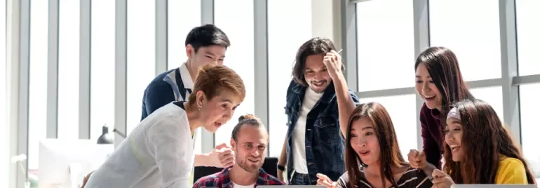 Group of people excitedly gathered around a laptop.