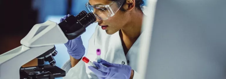 Scientist examining samples under a microscope in a lab.