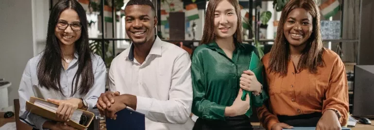 Four colleagues smiling and holding folders in an office setting.