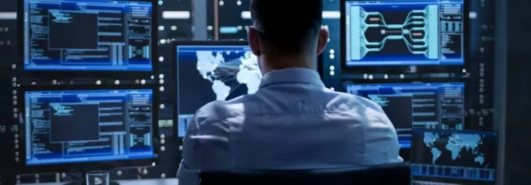 Person working in a data center, using multiple monitors displaying code and world maps.