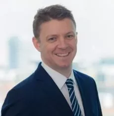 Smiling man in a suit with a city skyline in the background.