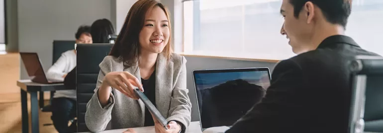Two professionals talking at a table in an office setting.