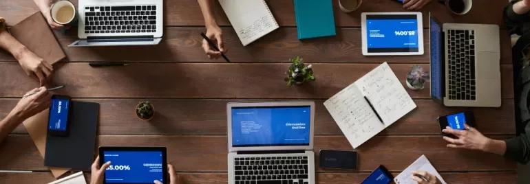 People working on laptops and tablets at a wooden table.