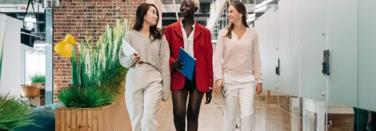 Three professionals walking in a modern office corridor with brick and glass walls.
