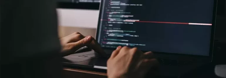 Person typing code on a laptop with a dark screen.