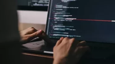 Person typing code on a laptop with a dark screen.