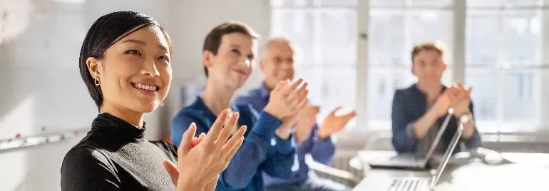 Group of people clapping during a meeting in a bright office.