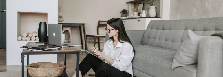 Woman sitting on floor by couch, working on laptop.